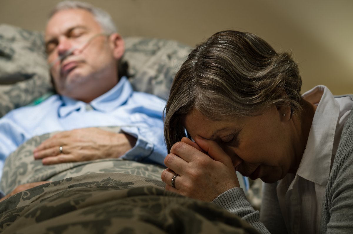 senior-woman-praying-for-sick-man-sleeping-in-hospital-bed.jpg